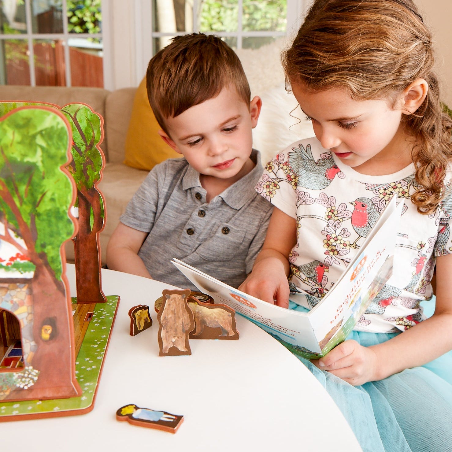 Two children sitting at a table with a book and wooden toys.